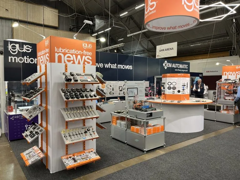 igus mässmonter med orange rundskylt och produktställ, byggd av Wilzéns Expo